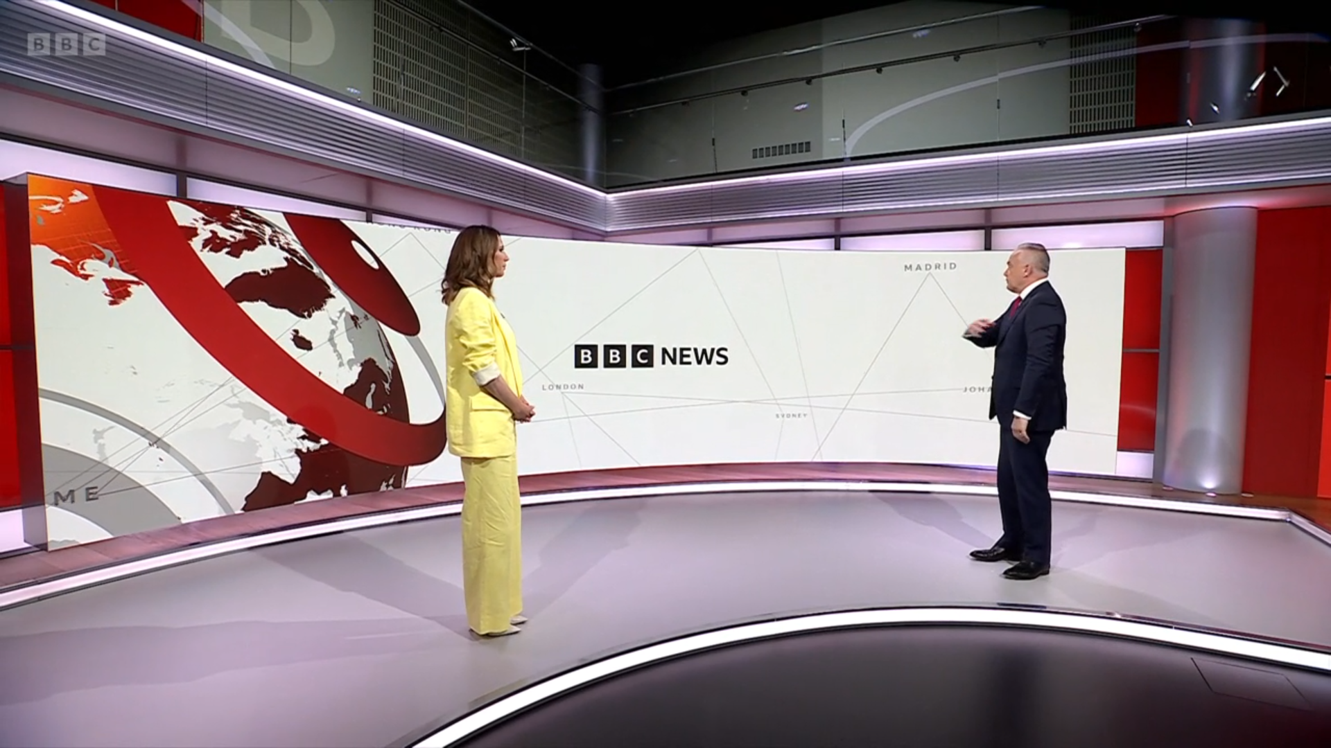 The catwalk area of the new BBC News set, with a large, continuous curved screen. Alex Jones is stood at the interview point, as directed by Huw Edwards.